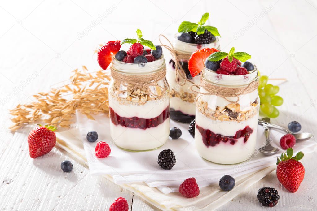 Tasty yoghurts with muesli, fresh berries and jam on wooden table.