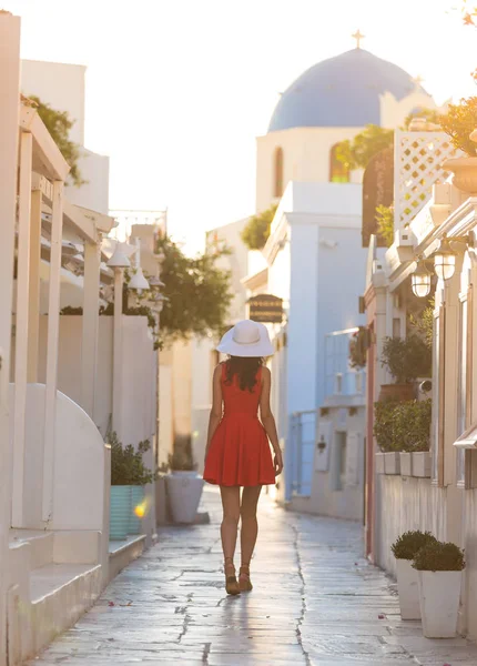 Santorini seyahat ediyor. Kırmızı elbiseli esmer kadın ünlü beyaz Oia köyünü ziyaret ediyor.. — Stok fotoğraf