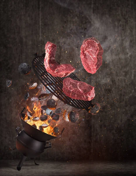 Parrilla para hervidor con briquetas calientes, rejilla de hierro fundido y sabrosos filetes de ternera volando en el aire . — Foto de Stock