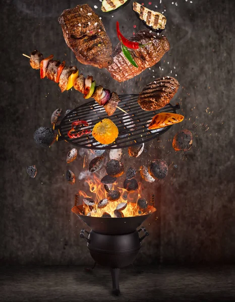 Grelha de chaleira com briquetes quentes, grelha de ferro fundido e carnes saborosas voando no ar . — Fotografia de Stock