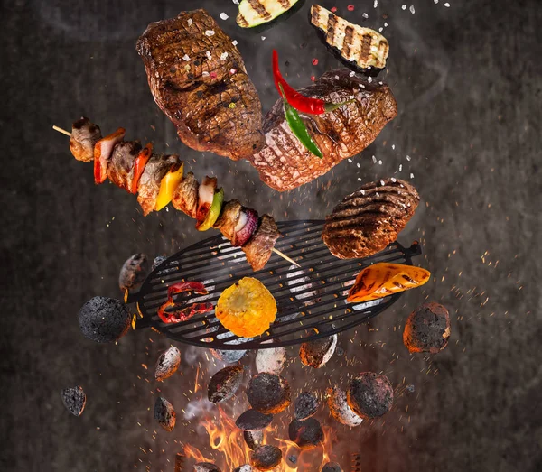 Grelha de chaleira com briquetes quentes, grelha de ferro fundido e carnes saborosas voando no ar . — Fotografia de Stock