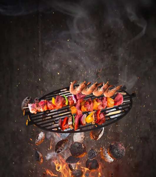 Kesselgrill mit heißen Briketts, gusseisernem Rost und schmackhaften Spießen, die in der Luft fliegen. — Stockfoto