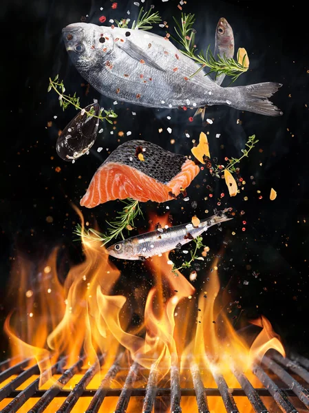 Tasty fishes flying above cast iron grate with fire flames. — Stock Photo, Image