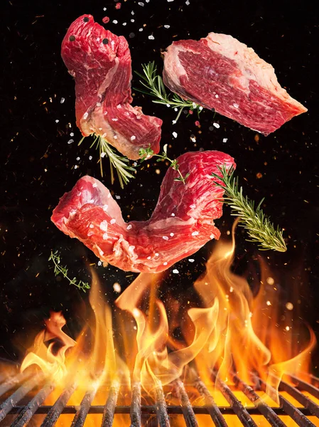 Tasty beef steaks flying above cast iron grate with fire flames. — Stock Photo, Image