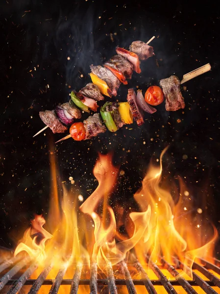 Tasty skewers flying above cast iron grate with fire flames. — Stock Photo, Image