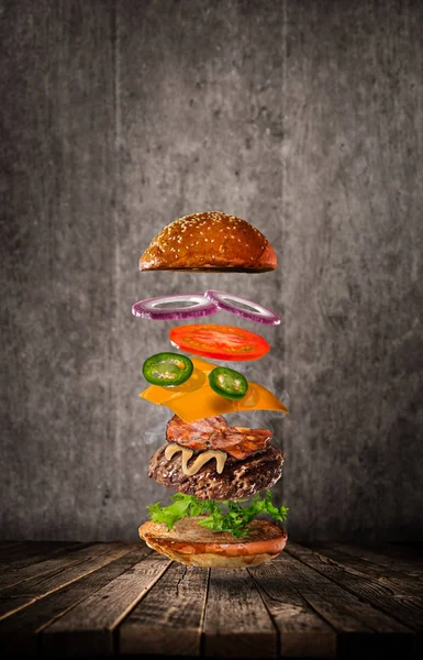 Hambúrguer saboroso com ingredientes voadores no fundo escuro — Fotografia de Stock