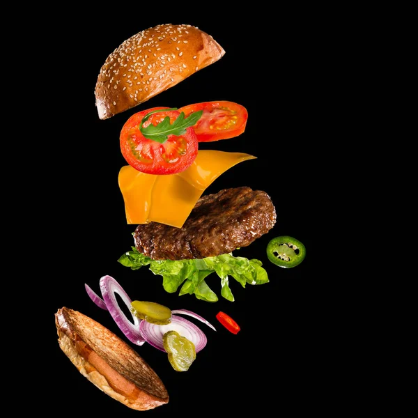 Gustoso hamburger con ingredienti volanti su sfondo scuro — Foto Stock