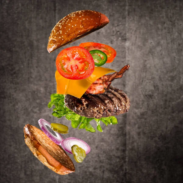 Gustoso hamburger con ingredienti volanti su sfondo scuro — Foto Stock