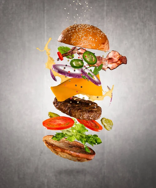 Вкусный чизбургер с летящими ингредиентами на тёмном фоне — стоковое фото