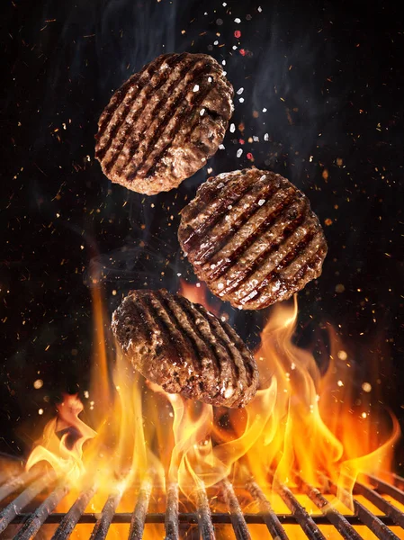 Bifes de carne saborosos voando acima grade de ferro fundido com chamas de fogo. — Fotografia de Stock