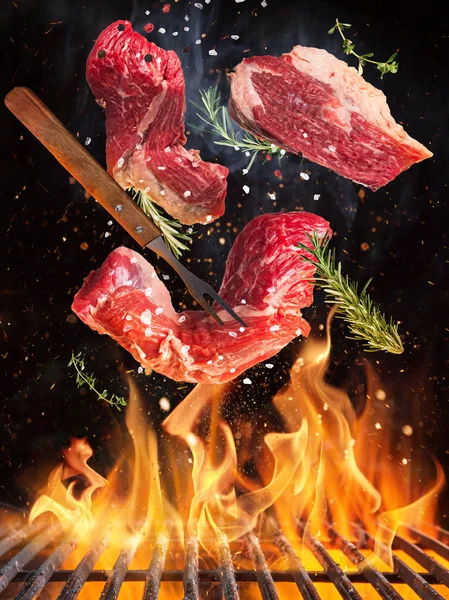 Bifes de carne saborosos voando acima grade de ferro fundido com chamas de fogo. — Fotografia de Stock
