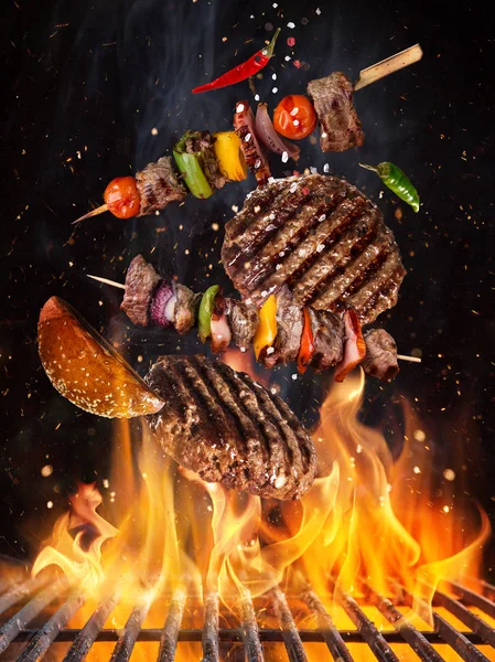 Tasty beef steaks and skewers flying above cast iron grate with fire flames. — Stock Photo, Image