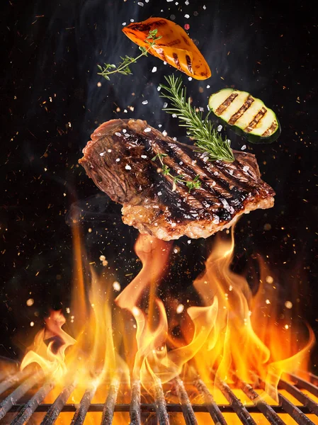 Tasty beef steaks flying above cast iron grate with fire flames. — Stock Photo, Image