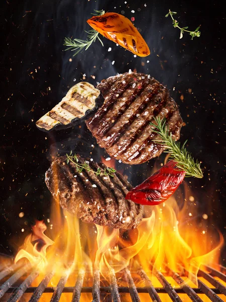 Tasty beef steaks flying above cast iron grate with fire flames. — Stock Photo, Image