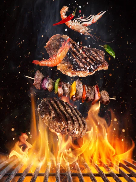 Sabrosos filetes de ternera y pinchos volando por encima de la rejilla de hierro fundido con llamas de fuego . — Foto de Stock