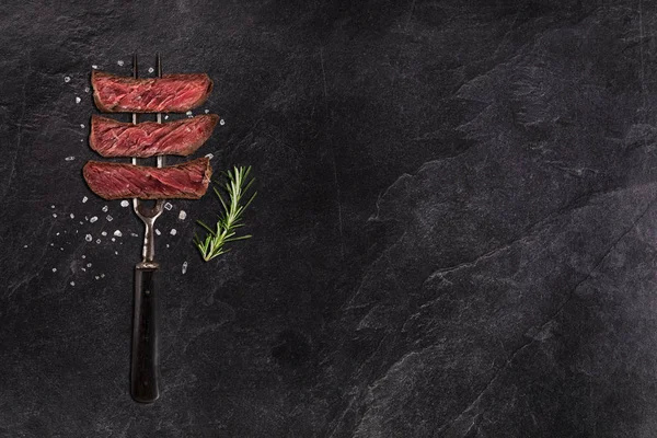 Sliced grilled beef steak with fork on black stone table — Stock Photo, Image