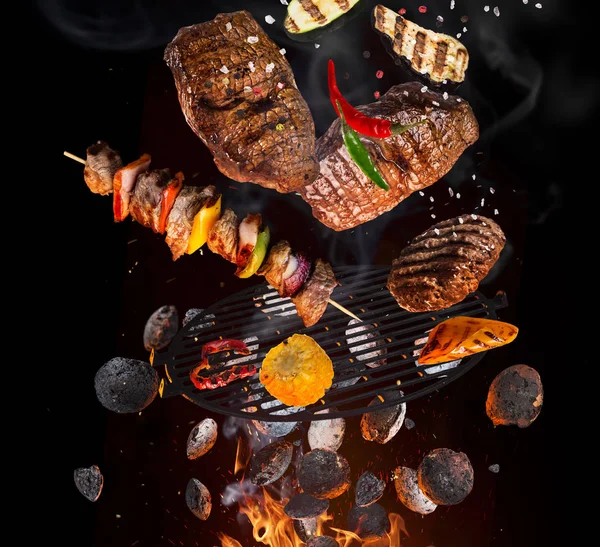 Смачні яловичі стейки та шампури, що летять над чавунною решіткою з вогнем . — стокове фото
