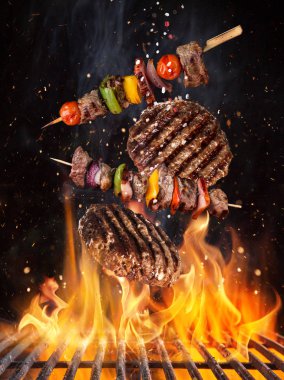 Lezzetli biftekler ve şişler havada uçuşuyor demir ızgarayı ateşle yakıyor.