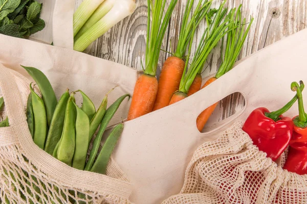 Légumes frais dans des sacs en coton bio sur une vieille table en bois . — Photo