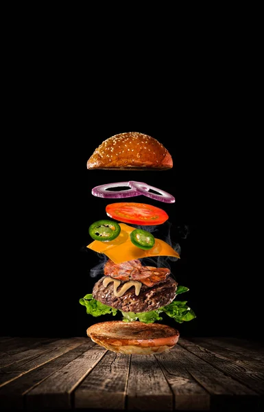 Hambúrguer saboroso com ingredientes voadores no fundo escuro — Fotografia de Stock
