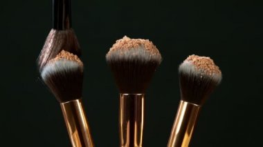 Makyaj fırçaları koyu arka plan ve küçük kozmetik parçacıkları, yavaş çekim birbirine dokunur.