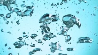 Sudaki çeşitli hava kabarcıklarının makro çekimi açık mavi arka planda yavaş çekimde yükseliyor