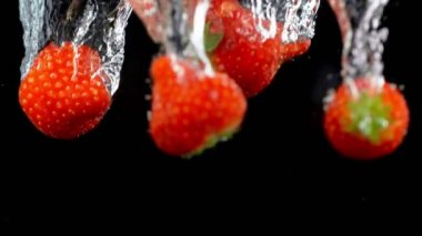 Siyah arka planda suyla patlayan çilekler..