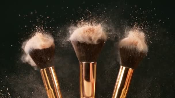 Los cepillos de maquillaje se tocan entre sí en el fondo oscuro y pequeñas partículas de cosméticos, cámara lenta. — Vídeos de Stock