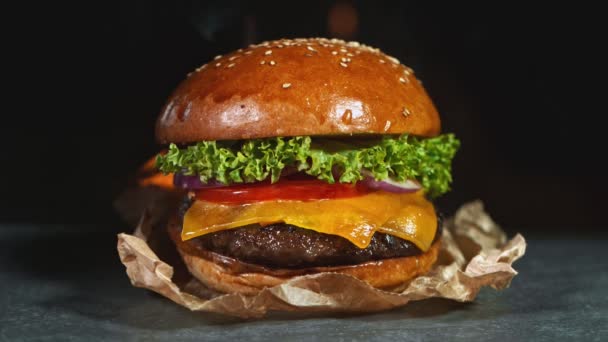 Cheeseburger gustos, culcat pe o placă de tăiere din lemn de epocă cu flăcări de foc în fundal. Super Slow motion — Videoclip de stoc