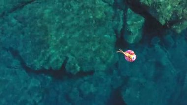 Suda mayo giymiş, şişme donut yüzüğünün üzerinde rahat genç bir kadın..