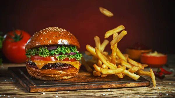 Franse frietjes vallen naast cheeseburger, liggend op vintage houten snijplank. — Stockfoto