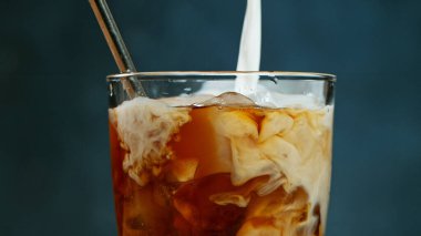 Buzlu kahvenin içine gri arka planda süt dökmek