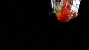 Siyah arka planda suyla patlayan çilekler..