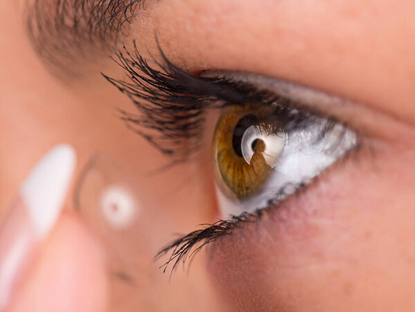 Young woman putting contact lens in her eye.