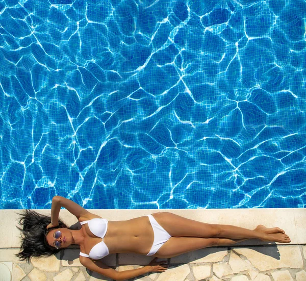 Bella donna con un cappello seduta sul bordo della piscina — Foto Stock