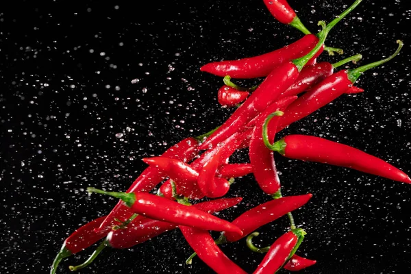 Färsk mogen röd chili paprika flyger på en svart bakgrund. — Stockfoto