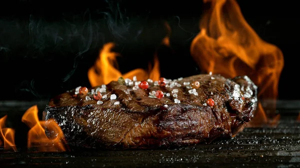 Tasty beef steak on cast iron grate with fire flames. — Stock Photo, Image