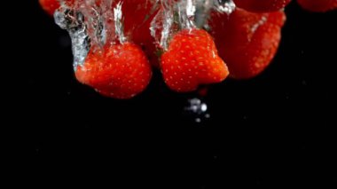 Siyah arka planda çilekleri suya düşürmek.