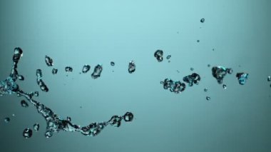 Mavi arka planda su sıçraması, süper yavaş çekim. Yüksek hızlı sinema kamerasıyla çekilmiş..