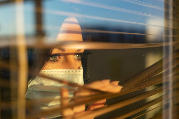 Женщина с вуалью, выглядывающей из окна дома, концепция карантина во время вирусной пандемии.