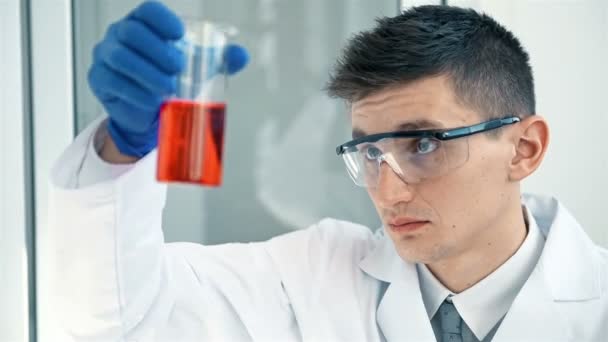 科学家在白色实验室外套 蓝色手套检查看烧瓶与红色液体在他的手臂 — 图库视频影像