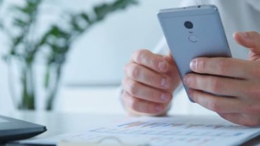 Ofiste oturan borsacı akıllı telefondaki iş raporlarını kontrol ediyor. Finans ve ticaret konsepti. Yavaş Hareket Efekti.