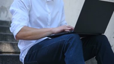 Merdivenlerde oturan ve dizüstü bilgisayarda yazan adam. İş ve Eğitim Konsepti. Kapat.