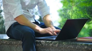 Öğrenci parkta oturuyor ve dizüstü bilgisayarla çalışıyor. Eğitim ve Çalışma Konsepti. Yavaş Hareket Efekti