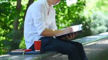 Genç iş adamı parkta oturuyor ve hisse senedi belgelerini analiz ediyor. Ticaret ve Başarı Konsepti.