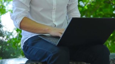 Öğrenci parkta oturuyor ve klavyede daktilo kullanıyor. Eğitim ve Çalışma Konsepti. Kapat.