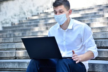 Laptop klavyesinde maske takan bir iş adamı. Pandemia covid konsepti. Kapat.