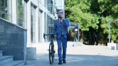 Bisikletli bir tüccar iş üstünde yürüyor ve cep telefonuyla konuşuyor. İş ve Yönetim Konsepti. Yavaş Hareket Efekti