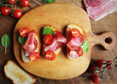 Bruschetta prosciutto jambon, domates ve yeşil ıspanak kesme tahtası üzerinde. Üstten görünüm .