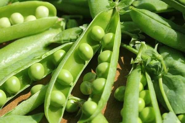 Ripe pods of green peas, fresh green peas on wooden table, close up .